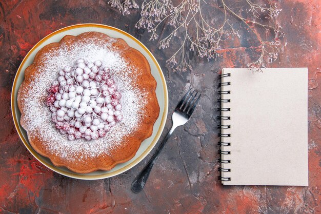 Bovenaanzicht van een cake een vork wit notitieboekje naast de smakelijke cake met rode aalbessen