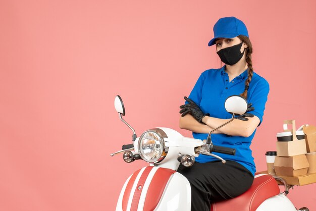 Bovenaanzicht van een denkende koeriersvrouw met een medisch masker en handschoenen die op een scooter zit en bestellingen aflevert op pastel perzik