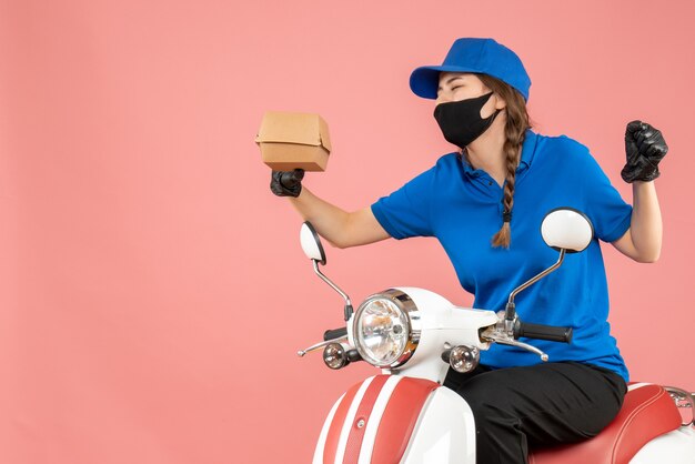 Bovenaanzicht van een emotionele bezorger met een medisch masker en handschoenen die op een scooter zit en bestellingen aflevert op een pastelkleurige perzikachtergrond