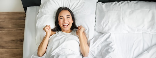 Gratis foto bovenaanzicht van een enthousiast aziatisch meisje dat in haar bed ligt en schreeuwt van vreugde en opwinding
