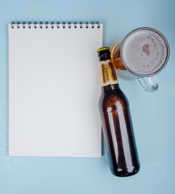 Bovenaanzicht van een flesje bier met een schetsboek en glas bier op blauw