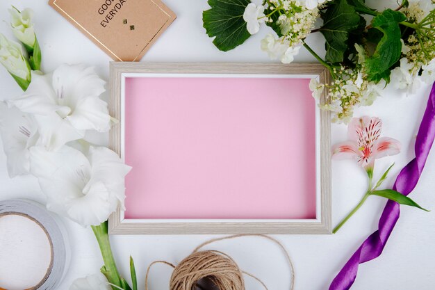Bovenaanzicht van een fotolijst met roze vel papier kleine briefkaart touw en witte kleur gladiolen bloem en een tak van bloeiende viburnum op witte achtergrond