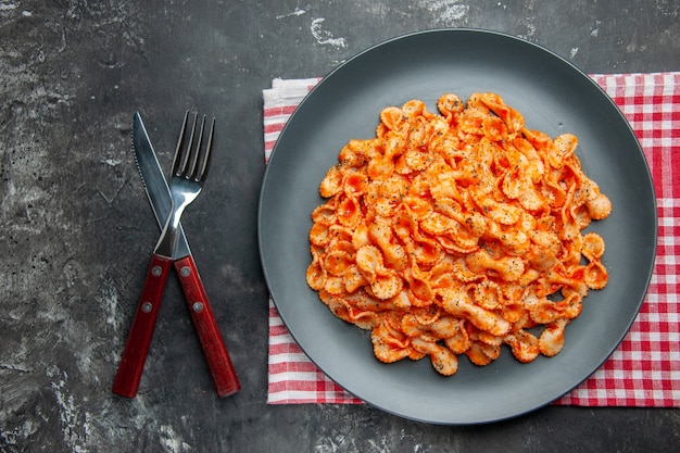 Bovenaanzicht van een gemakkelijke pastamaaltijd voor het diner op een zwarte plaat en bestek op een rode gestripte handdoek op een donkere achtergrond