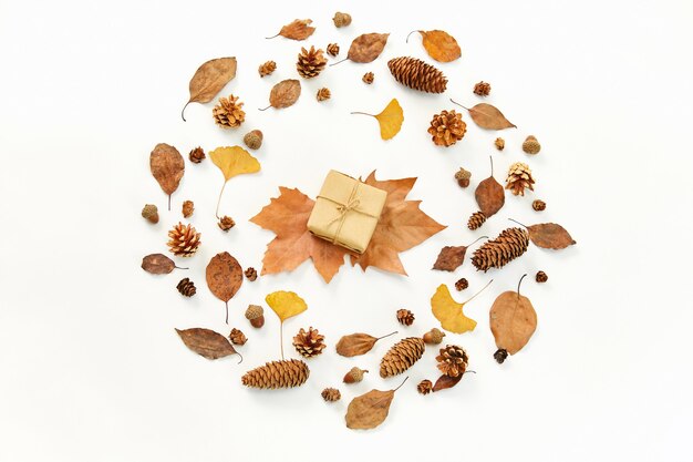 Bovenaanzicht van een geschenk in het midden van een krans gemaakt van herfstbladeren en coniferen op wit