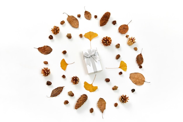 Bovenaanzicht van een geschenk in het midden van een krans gemaakt van herfstbladeren en coniferenkegels op wit