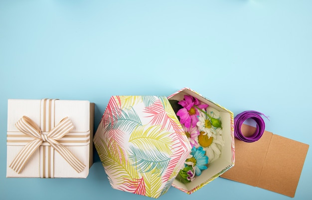 Bovenaanzicht van een geschenkdoos gebonden met strik en een geschenkdoos gevuld met kleurrijke chrysanthemum bloemen met madeliefje en paars lint met kleine ansichtkaart op blauwe achtergrond