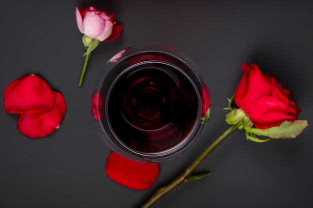 Bovenaanzicht van een glas wijn met rode kleur rozen op zwarte tafel