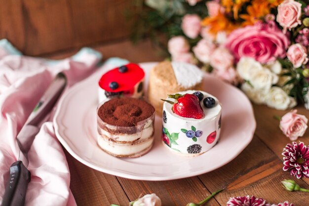 Bovenaanzicht van een heerlijke cake met kers op de top in de buurt van kleurrijke bloemdecoraties op een houten tafel