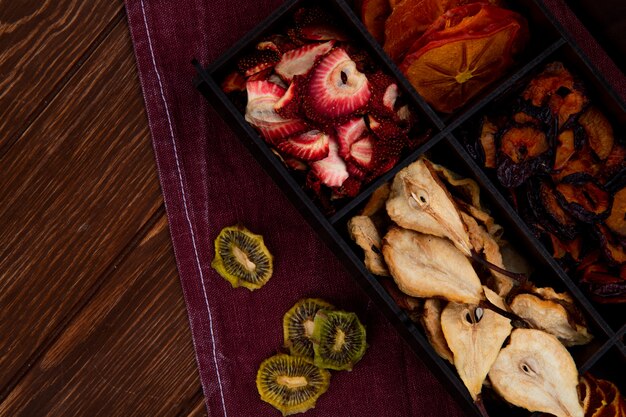 Bovenaanzicht van een houten kist met verschillende gedroogde vruchten peren aardbeien kiwi en pruimen plakjes op houten achtergrond met kopie ruimte