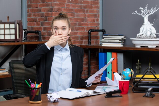 Bovenaanzicht van een jonge dame die aan een tafel zit en het document geeuwen op kantoor houdt