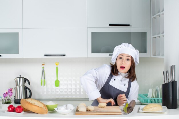 Bovenaanzicht van een jonge drukke vrouwelijke chef-kok in uniform die achter de tafel staat en gebak bereidt in de witte keuken