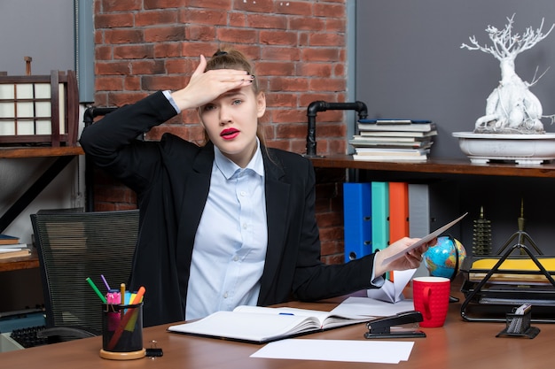 Bovenaanzicht van een jonge vrouw die aan een tafel zit en een document vasthoudt met hoofdpijn op kantoor