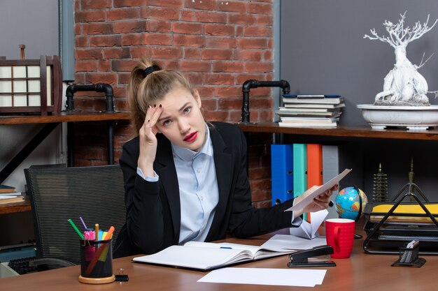 Bovenaanzicht van een jonge vrouw in diepe gedachten die aan een tafel zit en een document op kantoor vasthoudt