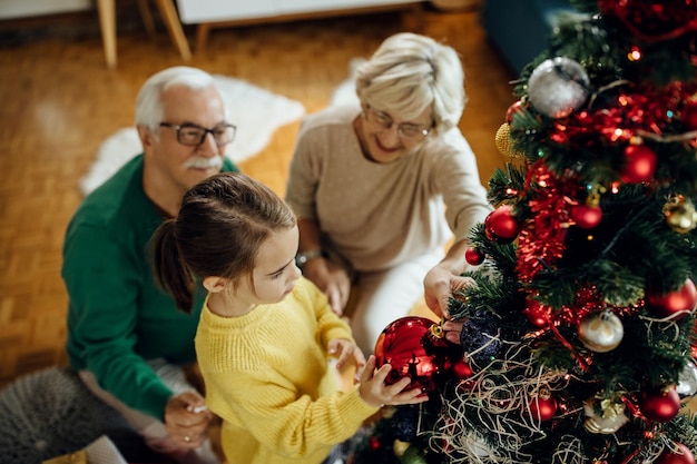 Bovenaanzicht van een klein meisje dat de kerstboom versiert met haar grootouders