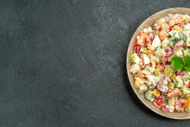 Bovenaanzicht van een kom groentesalade aan de rechterkant met groen erop op een donkergroene achtergrond