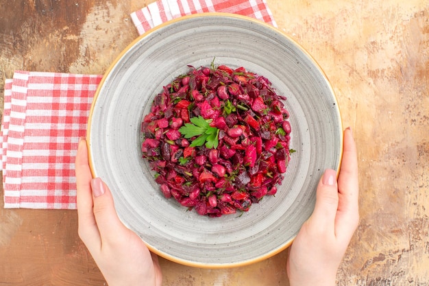 Bovenaanzicht van een kom met een rode salade met groenten erop op een ingecheckt servet op een houten backgorund