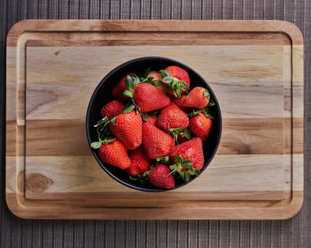 Bovenaanzicht van een kom met verse aardbeien op een houten snijplank