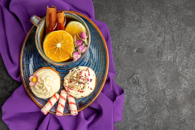 Bovenaanzicht van een kopje thee met citroenplaat van de smakelijke cupcakes en een kopje thee op het paarse tafelkleed aan de linkerkant van de tafel