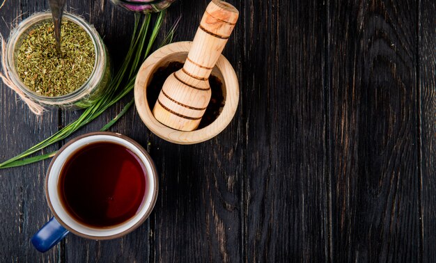 Bovenaanzicht van een kopje thee met gedroogde pepermunt in een glazen pot en zwarte peperkorrels in een houten vijzel op zwart hout met kopie ruimte