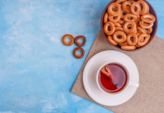 Bovenaanzicht van een kopje thee met kaneelstokje en een kom met brood ringen op blauwe achtergrond