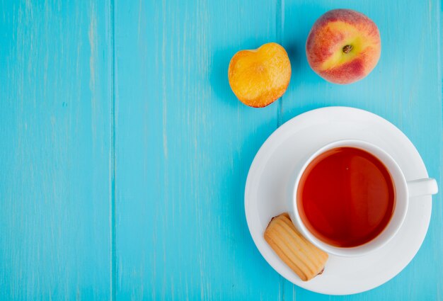 Bovenaanzicht van een kopje thee met koekje en verse rijpe perziken op blauw met kopie ruimte