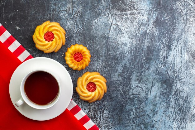 Bovenaanzicht van een kopje zwarte thee op een rode handdoek en koekjes aan de rechterkant op een donkere ondergrond