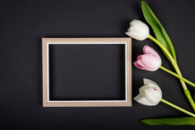 Bovenaanzicht van een leeg afbeeldingsframe en witte en roze kleur tulpen op zwarte tafel met kopie ruimte