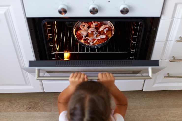 Gratis Foto bovenaanzicht van een meisjeskind dat de oven opent en kijkt naar smakelijke croissants of andere baksels in de oven, kookproces in de keuken, klein donkerharig vrouwelijk kind wil heerlijke snoepjes.