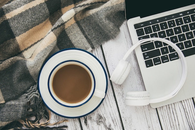 Bovenaanzicht van een moderne laptop met witte draadloze koptelefoon en een kopje koffie op tafel