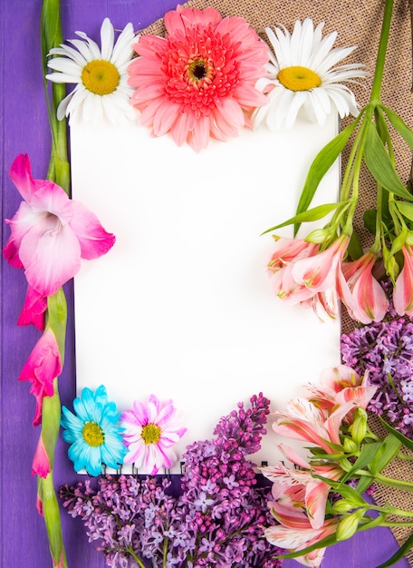 Bovenaanzicht van een schetsboek en roze en paarse bloemen gerbera lila alstroemeria en madeliefjebloemen op zak op paarse houten achtergrond