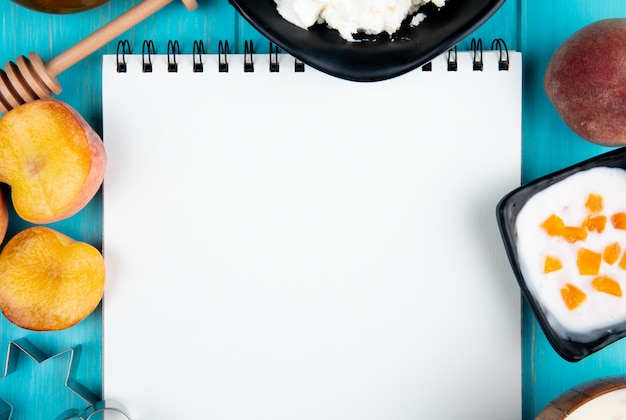 Bovenaanzicht van een schetsboek en verse rijpe perziken kwark yoghurt en cookie cutters gerangschikt op blauw