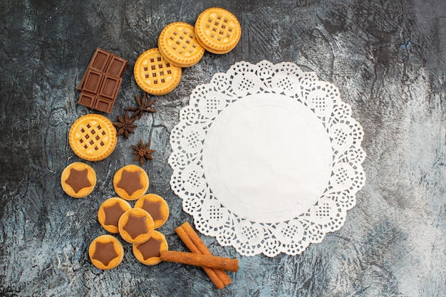 Bovenaanzicht van een stuk wit kant met koekjes en kaneel en chocolade op grijs