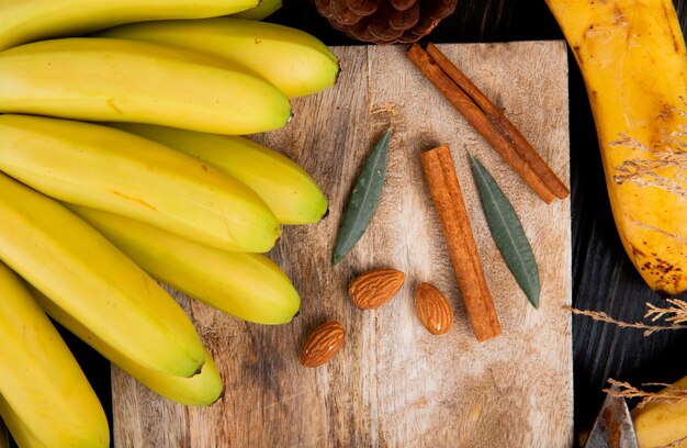Bovenaanzicht van een tros bananen met amandel en kaneelstokjes op een houten bord
