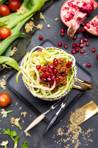 Bovenaanzicht van een veganistische maaltijd met spiraalvormige courgette, tomatensaus en granaatappels in de beker