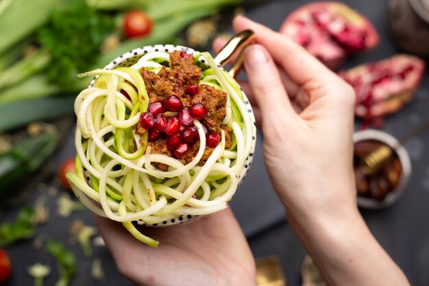 Bovenaanzicht van een veganistische maaltijd met spiraalvormige courgette, tomatensaus en granaatappels in de beker