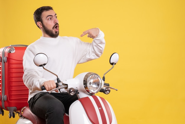 Bovenaanzicht van een verraste jonge kerel die op een motorfiets zit met een koffer erop en zichzelf op geel wijst