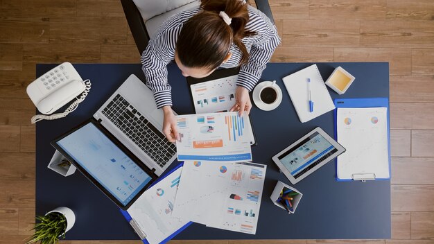 Bovenaanzicht van een zakenvrouw die aan een bureautafel zit en financiële boekhoudkundige documenten controleert