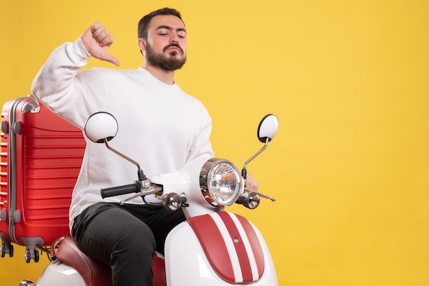 Bovenaanzicht van een zelfverzekerde jonge kerel die op een motorfiets zit met een koffer erop en zichzelf wijst op een geïsoleerde gele achtergrond