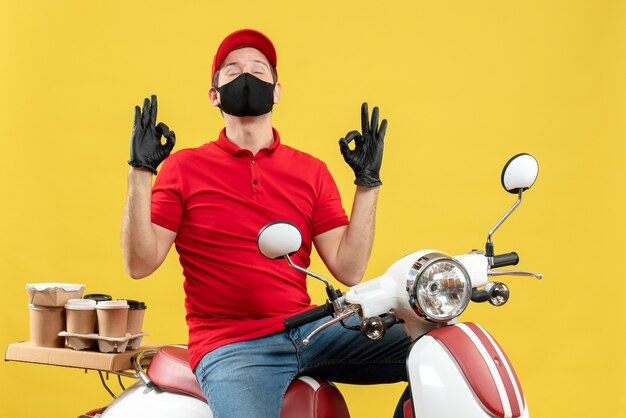 Bovenaanzicht van emotionele jonge volwassene dragen rode blouse en muts handschoenen in medisch masker leveren bestelling zittend op scooter dromen over iets
