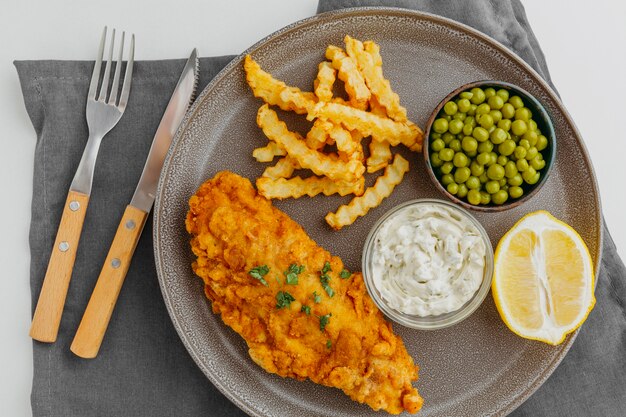 Bovenaanzicht van fish and chips op plaat met erwten en schijfje citroen