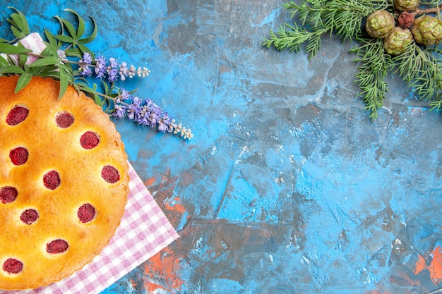 Bovenaanzicht van frambozencake op de vertakking van de de pijnboomboom van de keukendoek op blauwe oppervlakte