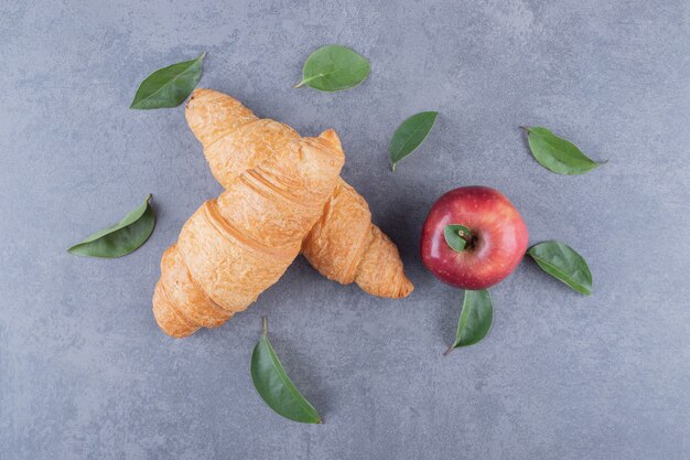 Bovenaanzicht van Franse croissants en verse appel op grijze achtergrond.