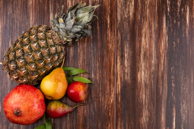 Bovenaanzicht van fruit als ananas, granaatappel en perzik op houten oppervlak met kopie ruimte