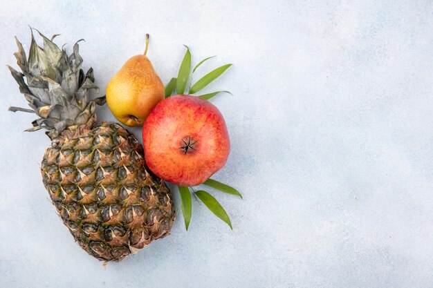 Bovenaanzicht van fruit als ananas, granaatappel en perzik op wit oppervlak met kopie ruimte