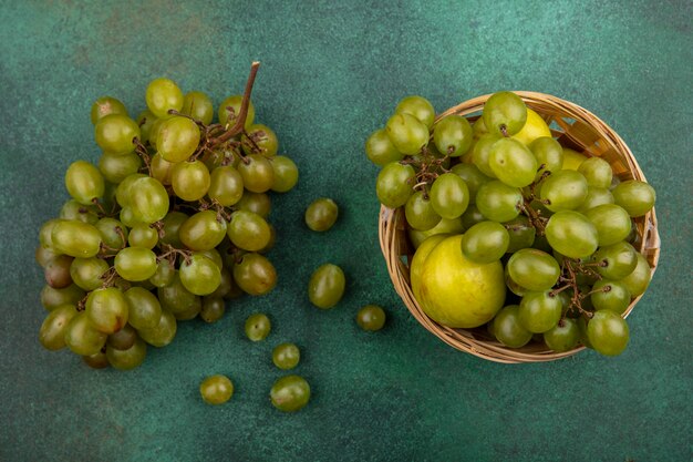 Bovenaanzicht van fruit als druif en pluot in mand en tros druiven op groene achtergrond