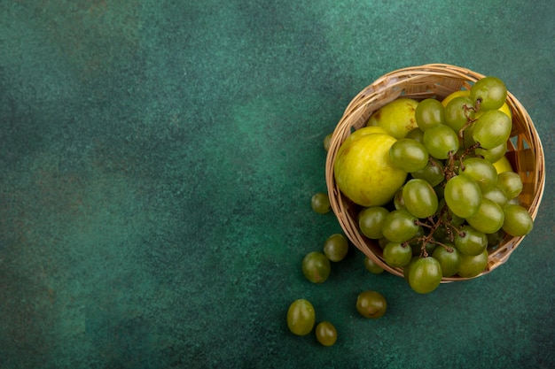 Bovenaanzicht van fruit als druif en pluot in mand op groene achtergrond met kopie ruimte