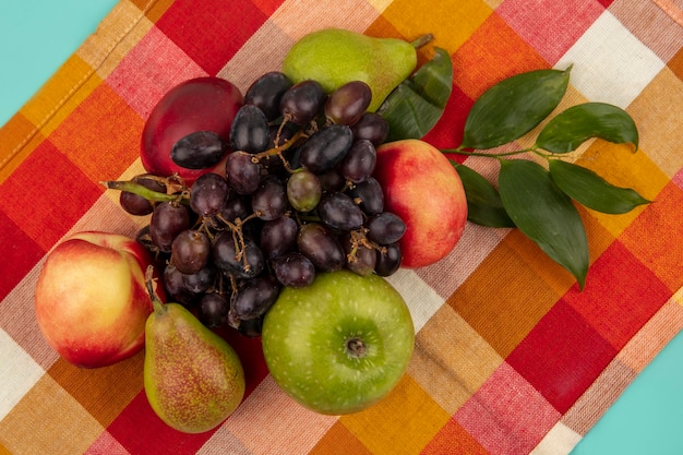 Bovenaanzicht van fruit als druiven perzik appel peer met bladeren op geruite doek achtergrond