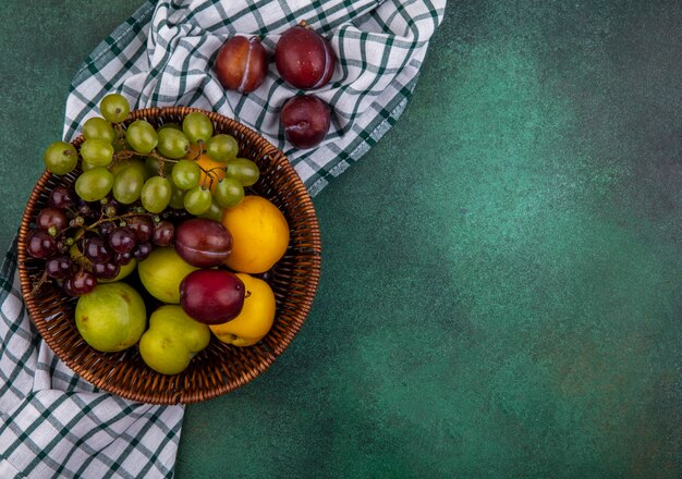 Bovenaanzicht van fruit als druivenplukken en nectacots in mand op geruite doek op groene achtergrond met kopie ruimte