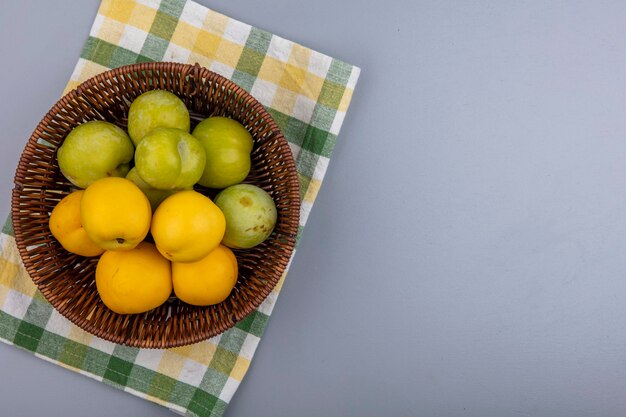 Bovenaanzicht van fruit als groene plukken en nectacots in mand op geruite doek op grijze achtergrond met kopie ruimte