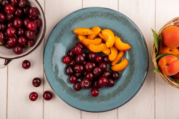 Bovenaanzicht van fruit als kersen en abrikozenplakken in plaat en mandje met abrikozen met kom met kersen op houten achtergrond